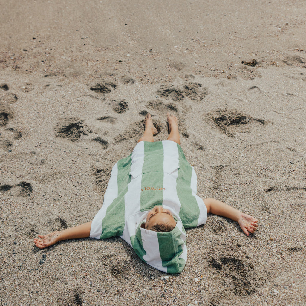 Child wearing a CRYWOLF hooded towel while lying on the beach.