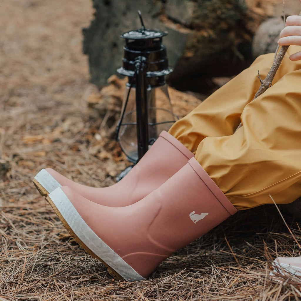 A Kid Sitting In The Forest Wearing Crywolf Rainboots Dusty Rose - Side View